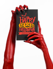 Postcard and Happy Halloween theme: red devil hand with black nails holding a paper card with the words Happy Halloween on a white isolated background in studio