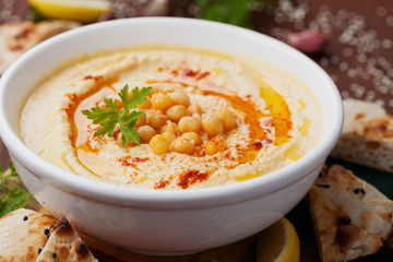 Hummus or houmous, appetizer made of mashed chickpeas with tahini, lemon, garlic, olive oil, parsley and paprika on wooden table