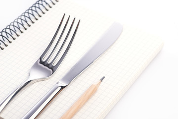 Fork, knife, notepad and pencil over the white background