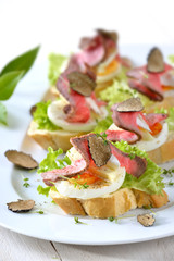 Garnierte Appetithäppchen mit Roastbeef,  schwarzer Herbsttrüffel, französischem Brie und Ei auf Baguette