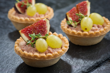 tartlets with liver pate and fruit on a dark background