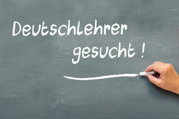 Hand writing on a chalkboard in German Deutschlehrer gesucht
