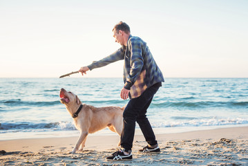 young caucasian male playing with labrador on beach during sunri