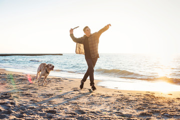 young caucasian male playing with labrador on beach during sunri