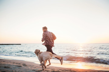 young caucasian male playing with labrador on beach during sunri
