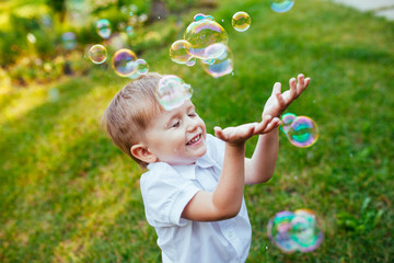 Little boy with soap bubbles in summer park.