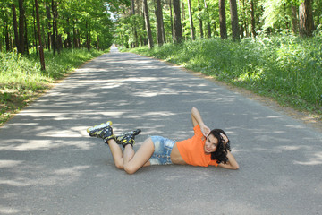 Portrait of positive crazy cheerful girl on roller skates. Young woman in roller skates, sitting on the road looking at camera and smiling. happy young brunette woman on roller skates in the park