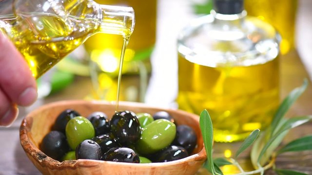 Olives and pouring olive oil. Extra virgin olive oil pouring from a jar