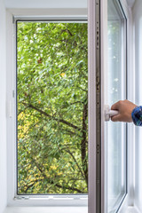 man opens pvc window, which you can see green of a tree park in the ecologically clean area of the...