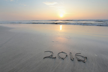 Sandy beach with 2016 written on sand with sunrise in background