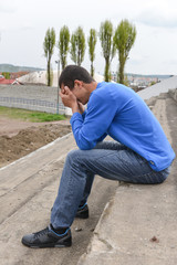 Upset teenager sitting on stairs laying his head on his hands