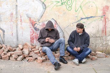 Two street hooligans or rappers sitting against a graffiti paint