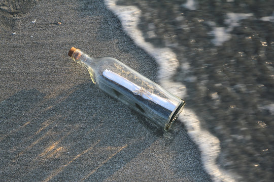 Message in a bottle on sandy beach during sunrise/sunset with moving waves