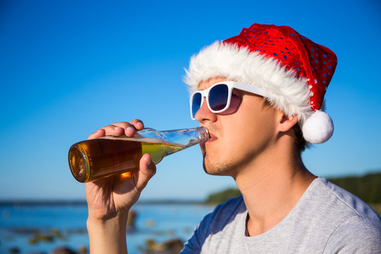 christmas concept - portrait of man in santa hat drinking beer o