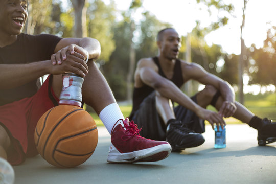 Two young men taking a water break while playing basketball in the park at sunset