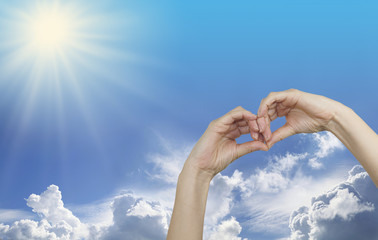 Looking for a sunny vacation - a pair of female hands making an eye mask shape with a blue sky and sunburst background plus copy space above