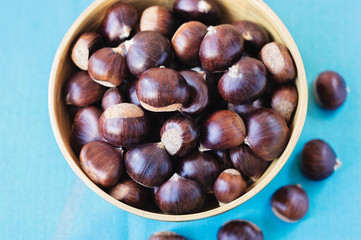 Bamboo bowl of fresh chestnuts on a blue background.