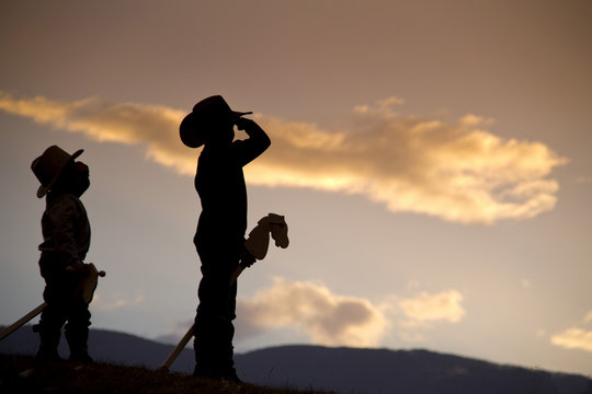 Silhouette of two boys with hobby horses pretending to be cowboys saluting with pride