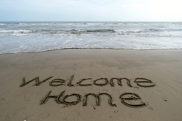 Fototapeta premium welcome home written in sand, with the sea in the background 