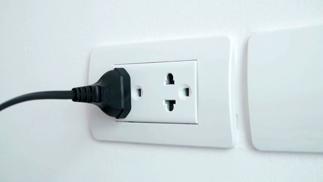 Left man hand plugging and unplugging electronic into electric wall socket. 