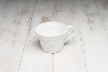 Fototapeta na wymiar Empty White Handmade Cup on White Wooden Panel Surface