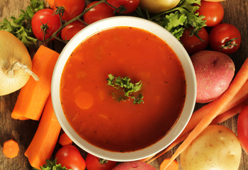 Vegetables soup surrounded by fresh vegetables on a wooden background