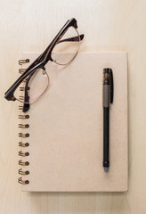 Brown notebook with eyeglasses and black pen on wood background