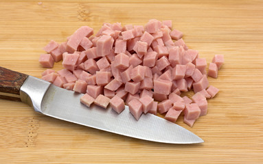 Diced ham on a wood cutting board with knife