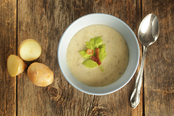 Top view of a potato soup in a blue bowl with fresh potatoes and spoon on a wooden background
