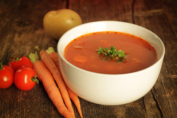 Vegetables soup surrounded by fresh vegetables on a rustic background