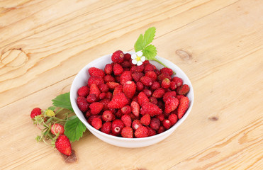 Delicious wild strawberries in a white bowl on wood