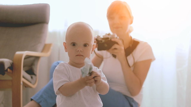 Mother taking a pictures using retro film camera of her baby boy in sunny living room.