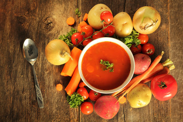 Vegetables soup surrounded by fresh vegetables and a spoon on a wooden background