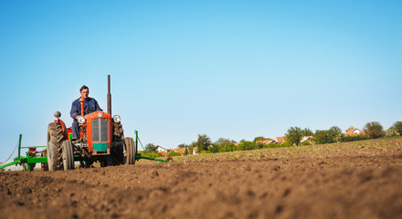 Farmer in Old-fashioned tractor sowing crops at field