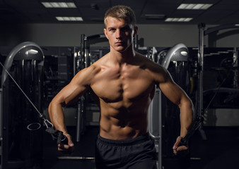 Young athletic man pumping up muscles on crossover