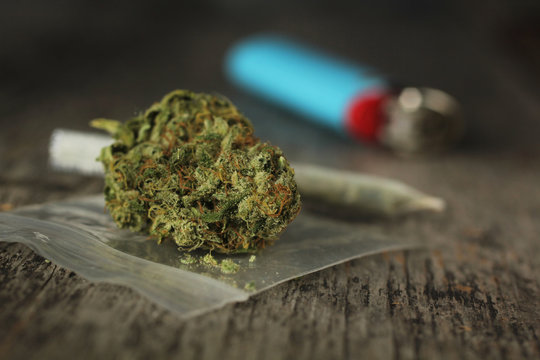 Closeup of marijuana joint and buds and blue lighter on a wooden table with a shallow depth of field
