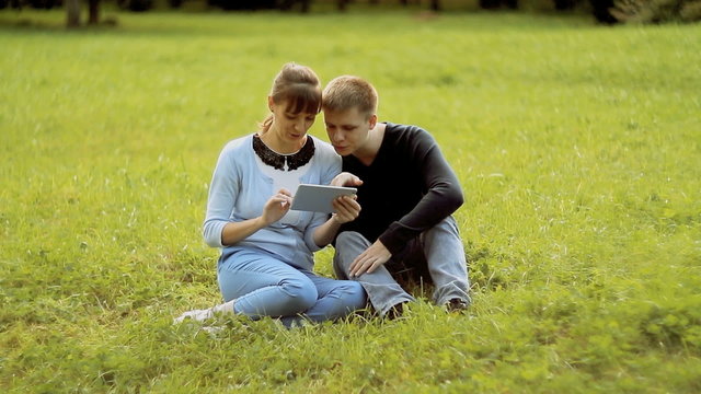 Young couple using tablet computer touchscreen in park 