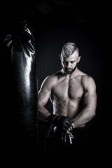 Obraz na płótnie Canvas Male Athlete boxer punching a punching bag with dramatic edgy li