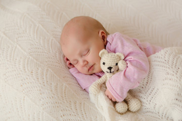 Neugeborenes Baby schläft zufrieden auf weisser Decke mit Teddy im Arm und lächelt