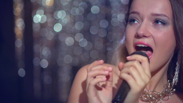 Beautiful girl with long blowing hair singing karaoke over glowing background