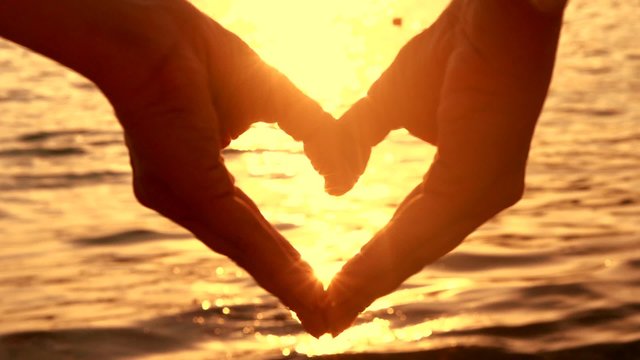 Ocean sun shining through heart shaped female hands