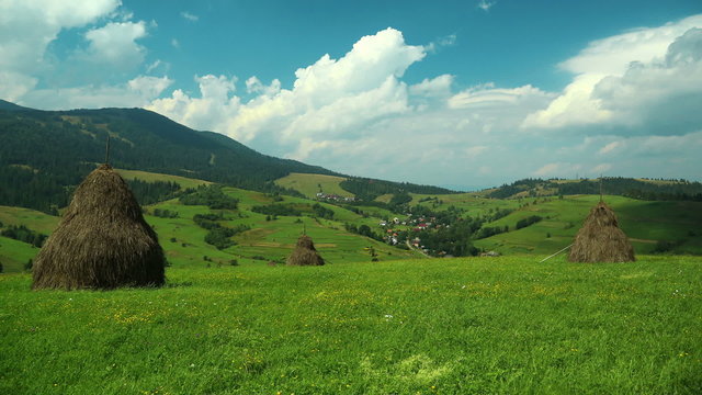 Time lapse of clouds and green fields with haystacks
