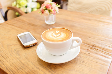 Cup of coffee latte art with mobile phone on wood table