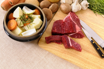 Preparing beef steak for casserole or stew with crock pot vegetable ingredients chopping board and knife photo