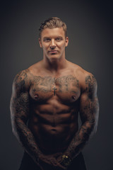 Fototapeta premium Portrait of muscular tattooed man in shadows isolated on grey background.