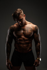 Portrait of muscular tattooed man in shadows isolated on grey background.