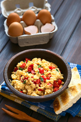 Scrambled eggs made with red bell pepper and green onion in rustic bowl, photographed with natural light (Selective Focus, Focus one third into the scrambled eggs)