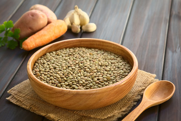 Raw lentils (lat. Lens culinaris) in wooden bowl, photographed on dark wood with natural light (Selective Focus, Focus one third into the raw lentils)
