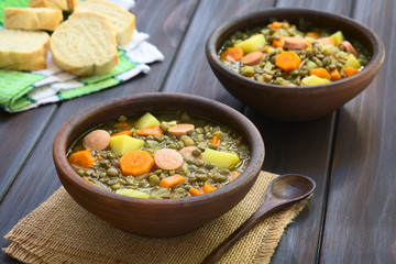 Lentil soup made with potato, carrot, onion and sausage slices, photographed 
with natural light (Selective Focus, Focus on the middle of the first soup)