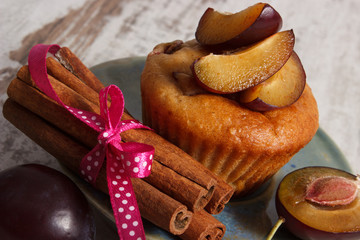 Fresh baked muffins with plums and cinnamon sticks on old wooden background, delicious dessert